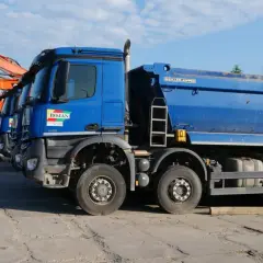 Niebieskie wywrotki i koparka stojące na placu budowy.