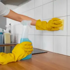 Osoba w żółtych rękawiczkach czyści białe płytki płynem do czyszczenia.